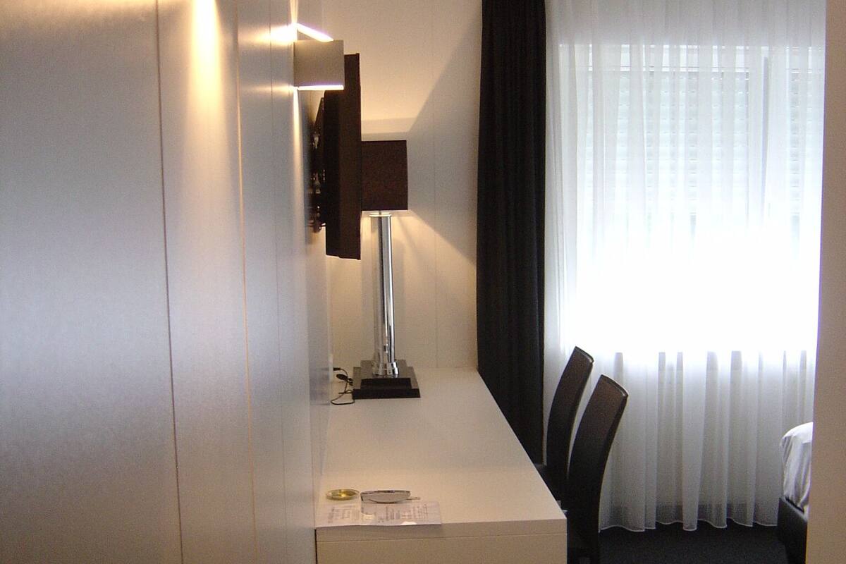 A hotel room with a desk, a chair, a lamp, and a window with curtains.