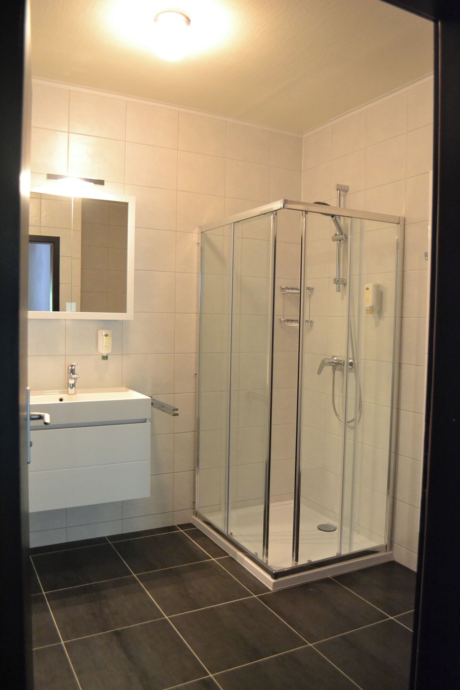 Un bagno moderno con cabina doccia in vetro, piastrelle bianche e un’area lavabo ben visibile.