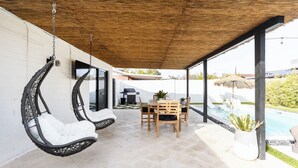 Un patio cubierto con sillas colgantes, una mesa con sillas y vistas a una piscina.