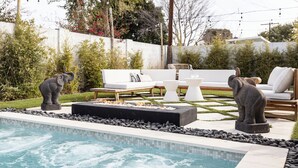 Una piscina con borde de piedra, un conjunto de sofás blancos y dos estatuas de elefantes.