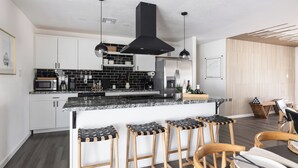 Una cocina moderna con armarios blancos, salpicadero negro y una isla central con taburetes de bar.