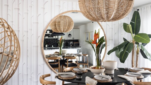Un área de comedor con un espejo redondo, mesa negra, sillas de madera y una planta central.