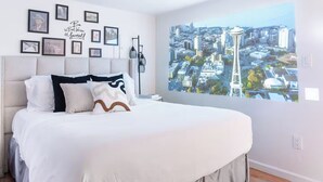 Een slaapkamer met een groot bed, een stadsgezicht muurschildering aan de muur en enkele ingelijste foto's.