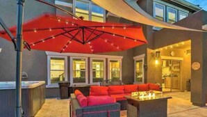 Une terrasse extérieure avec un parasol rouge, des meubles en osier et un foyer.