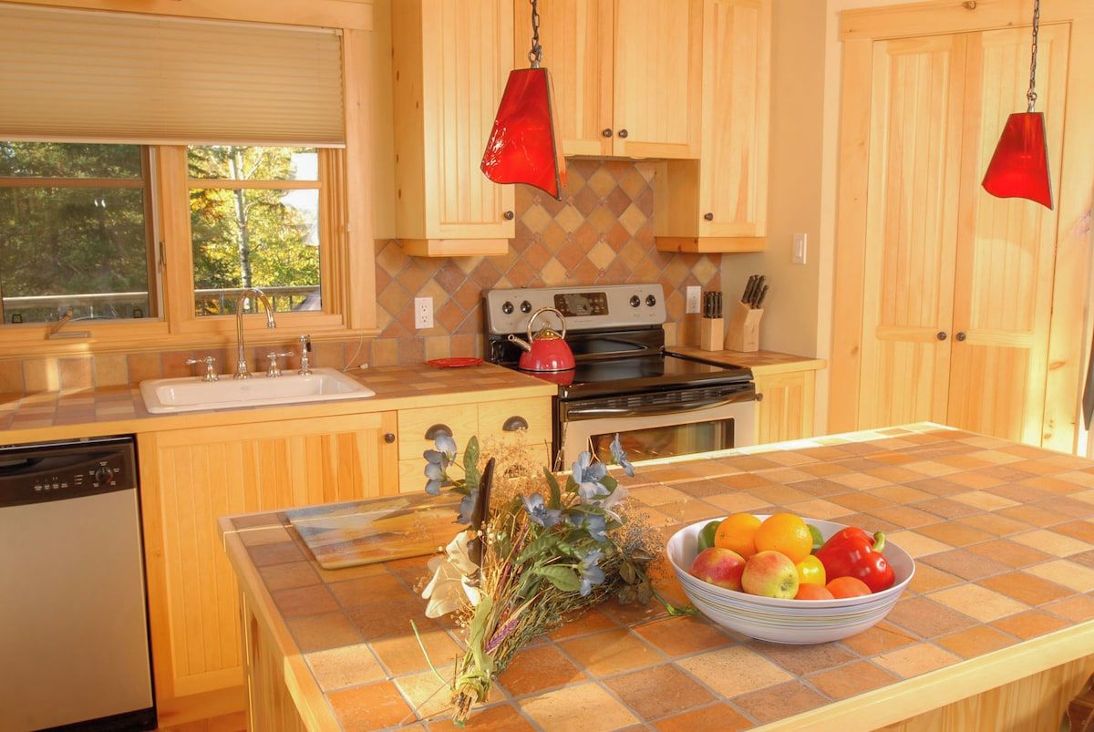 A kitchen with wooden cabinets, a stove, a sink, and a countertop with a bowl of fruit and flowers.