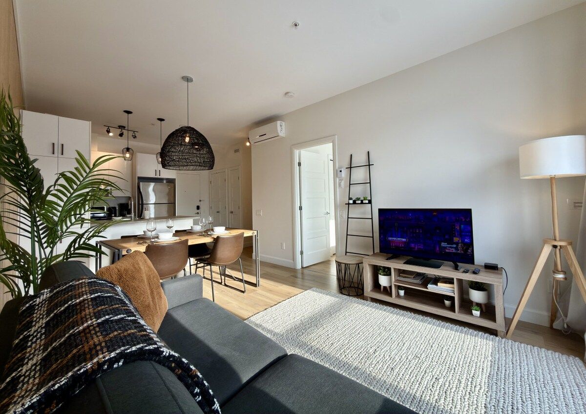 Een moderne woonkamer met een bank, een televisie en een eethoek met een tafel en stoelen.