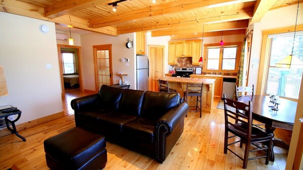 Una sala de estar acogedora con un sofá de cuero, pisos de madera y una zona de cocina con armarios de madera y una mesa de comedor.
