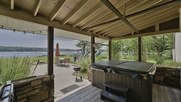 A covered outdoor patio with a hot tub, grill, and seating area overlooking a lake. - Hideaway Retreat at Pocono Summit Lake - Dock, Boats, Hot Tub & Sauna (Pocono Summit)