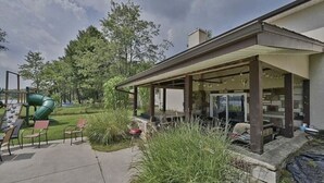 A covered patio area with outdoor seating, a barbecue grill, and a playground with a slide. - Hideaway Retreat at Pocono Summit Lake - Dock, Boats, Hot Tub & Sauna (Pocono Summit)