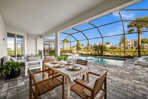 An outdoor patio with a pool, wooden furniture, and a view of the surrounding area. - Charming lakeside home with pool, spa  and modern coastal design. (Ave Maria)