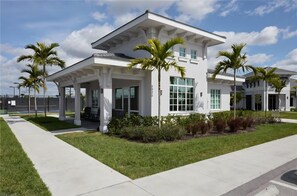 A modern two-story building with a covered patio area, palm trees, and a clear sky. - Charming lakeside home with pool, spa  and modern coastal design. (Ave Maria)