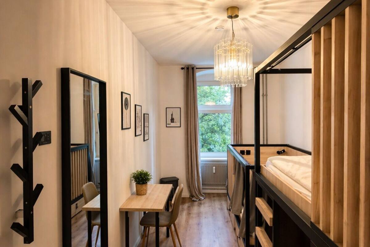 Una habitación pequeña con una cama nido, una mesa de comedor con sillas, una planta en maceta y un espejo en la pared.