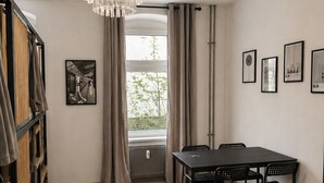 A room with a dining table, chairs, a chandelier, a radiator, a window with curtains, and a bookshelf. - Berlin Sleep Club (Berlin)