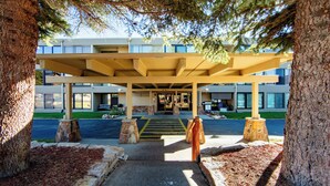 A building entrance with a covered walkway, stone bollards, and a parking lot. - Lld308-2 (Dillon)