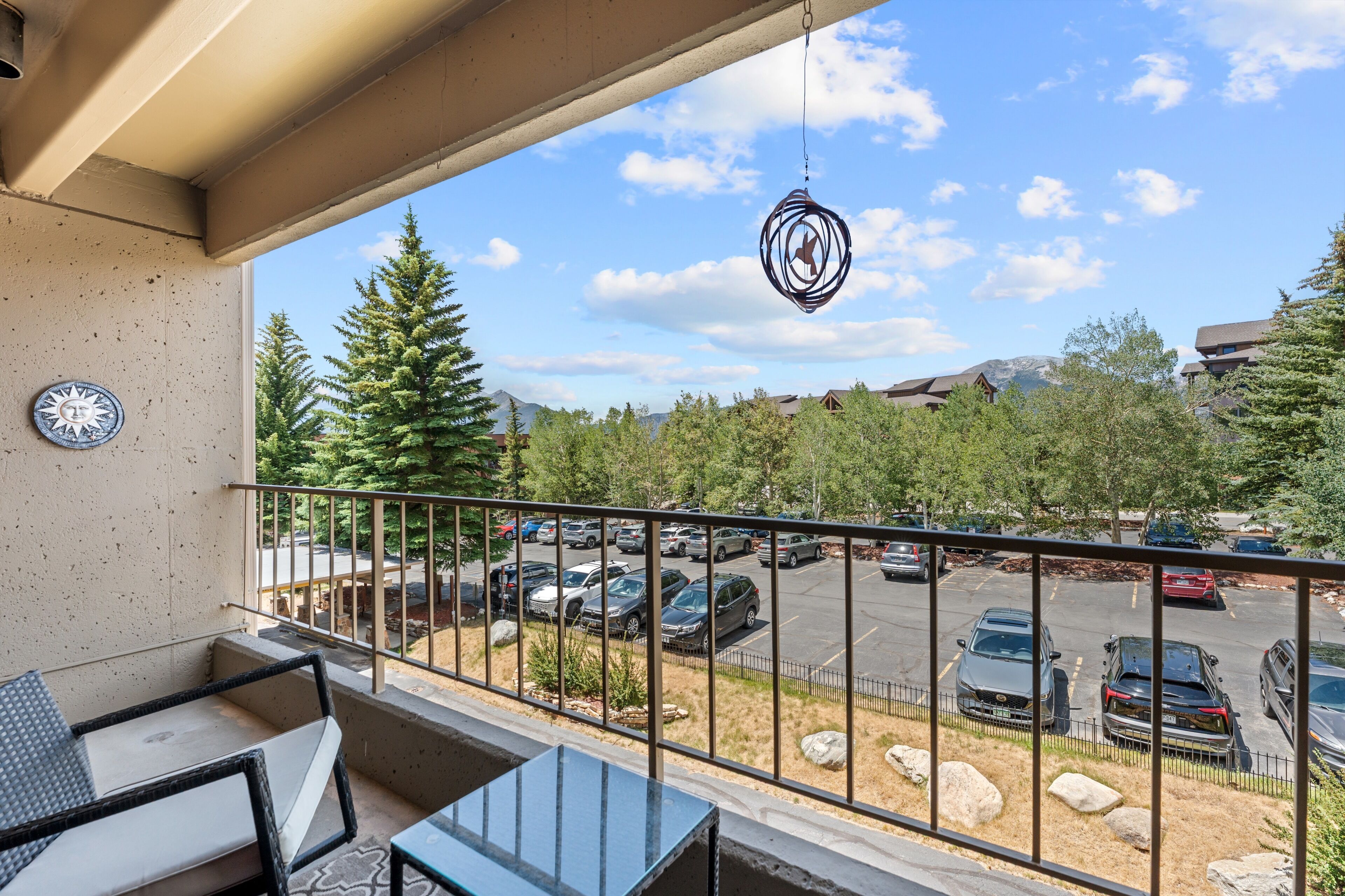 Un balcon donnant sur un parking, avec des arbres et des bâtiments en arrière-plan.