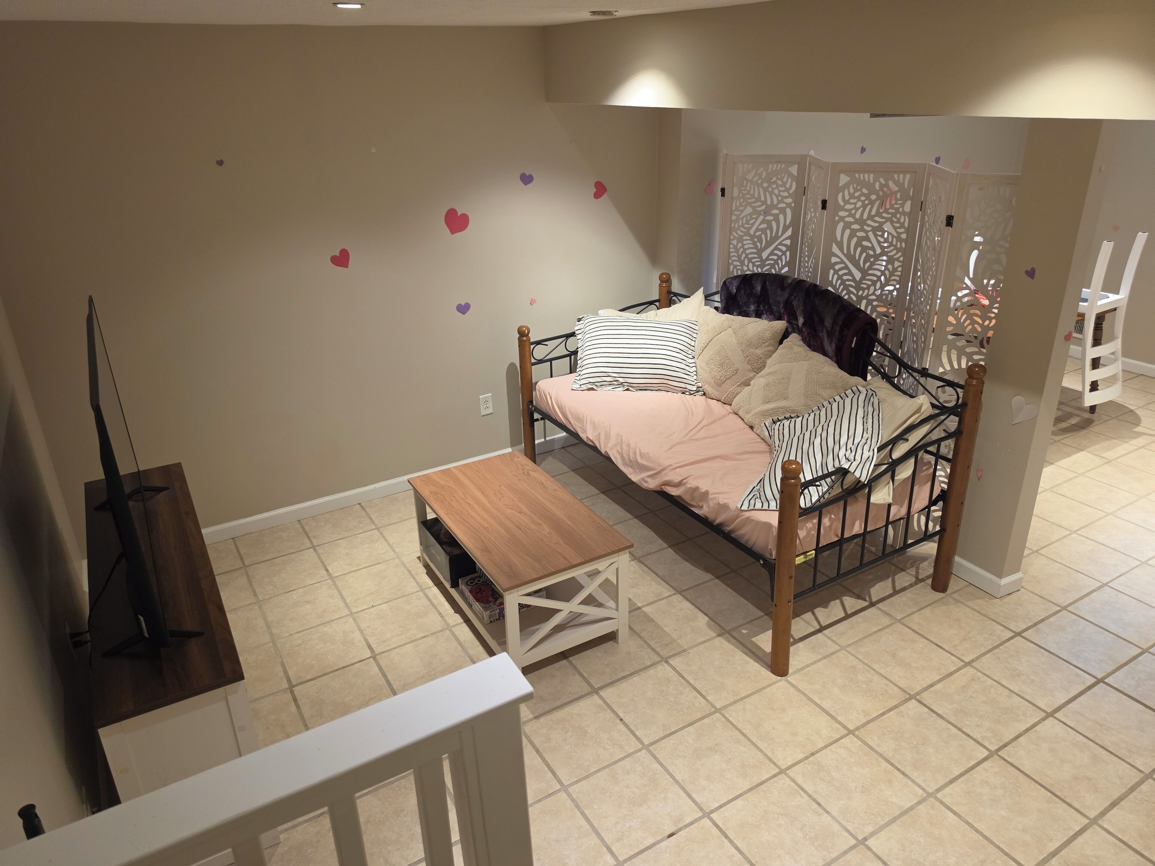 A bedroom with a bed, a wooden bedside table, a white chair, and a decorative wall with heart shapes.