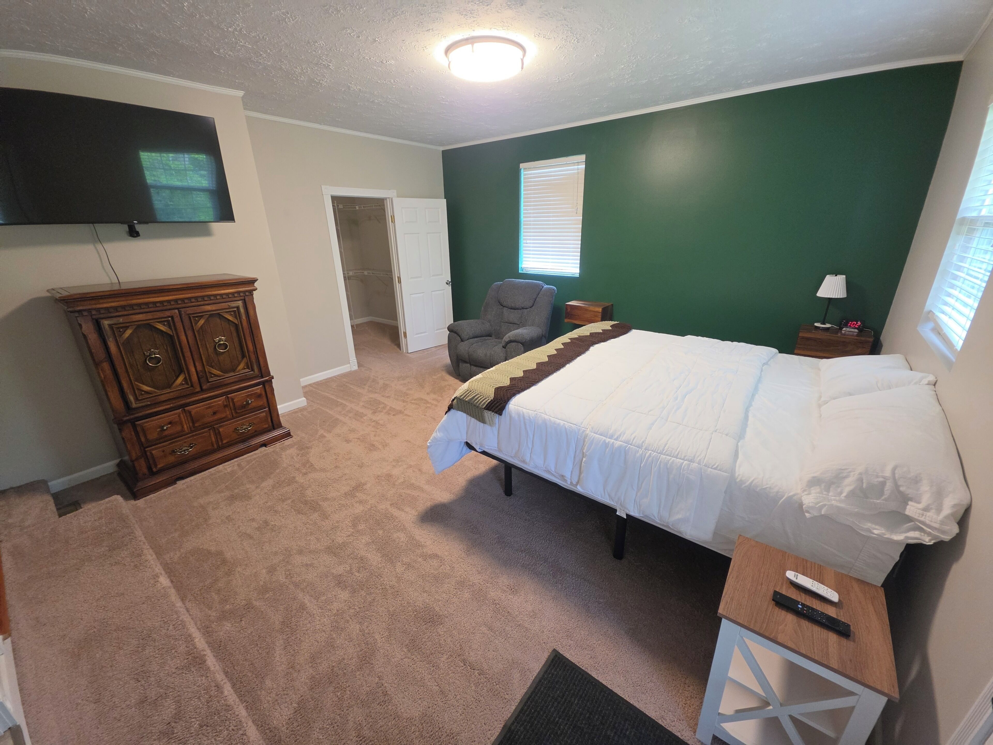 A bedroom with a bed, a dresser, a TV, a chair, and a window.