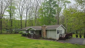 A small, single-story house with a front porch, a chimney, and a deck.