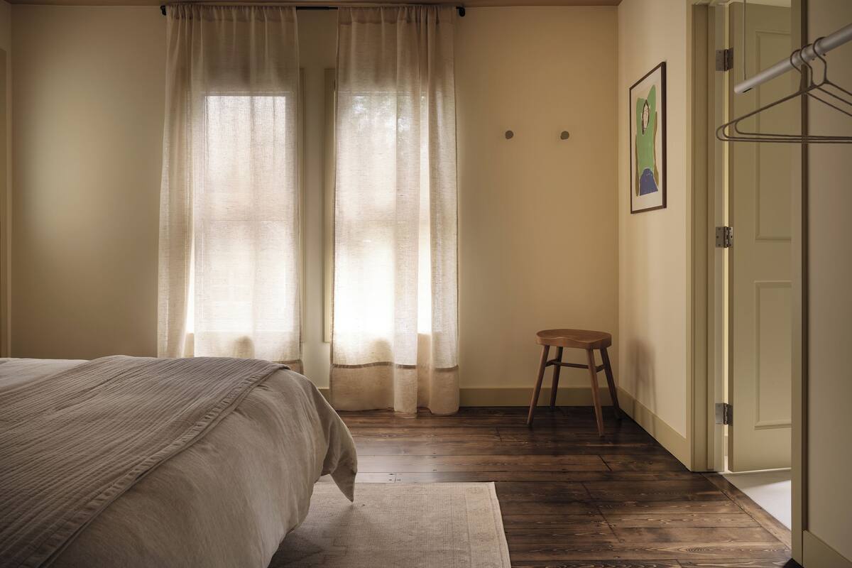 Un dormitorio con una cama, un taburete de madera y una puerta.
