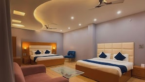 A modern hotel room with two beds, a sofa, a glass coffee table, and a ceiling fan. - ECHOS Hotel Rishikesh (Rishikesh)
