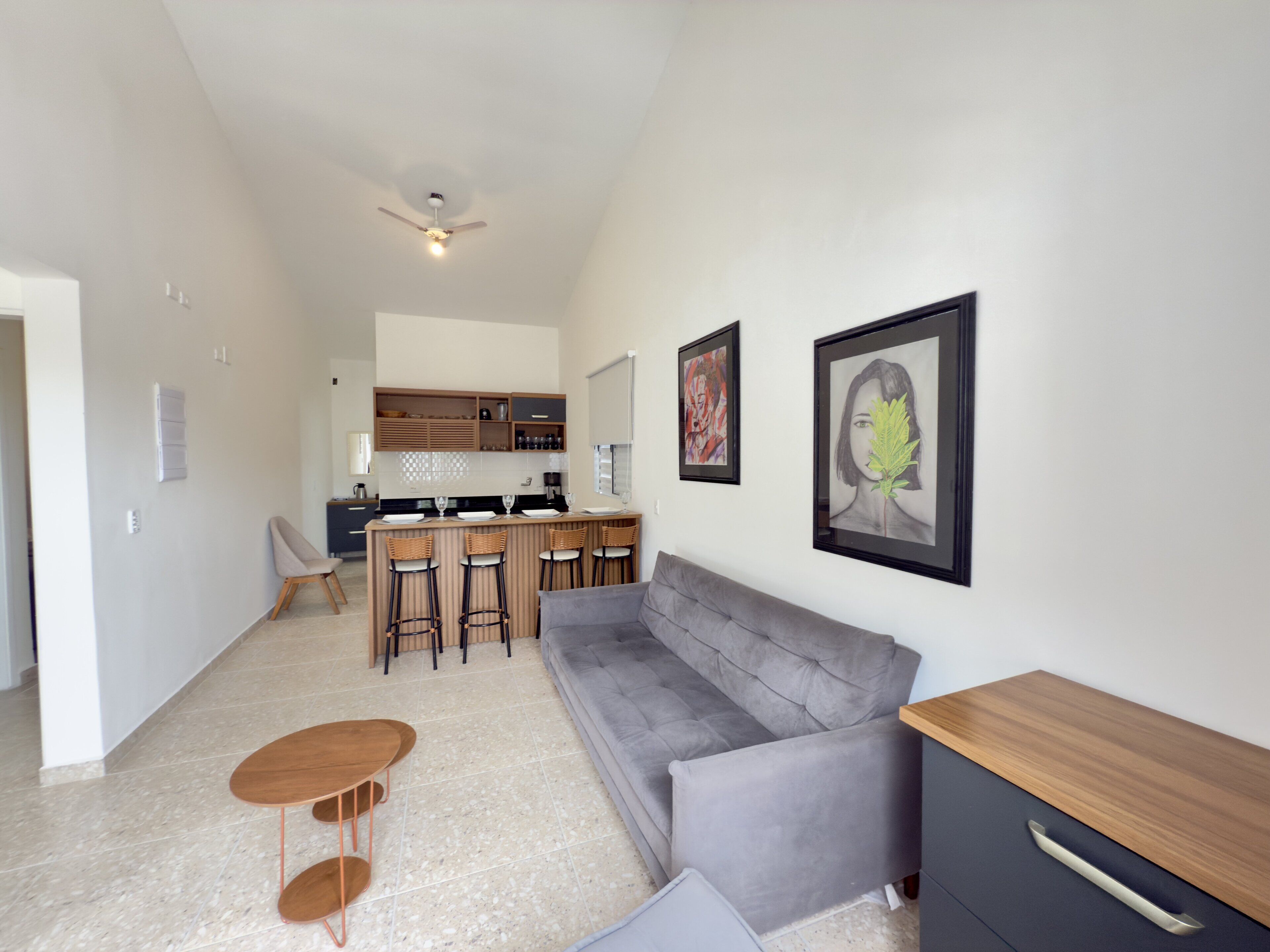 Una sala de estar moderna con un sofá gris, una mesa de centro de madera y una zona de cocina con barra y taburetes.