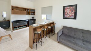 A modern kitchen with a central island, bar stools, and a grey sofa.