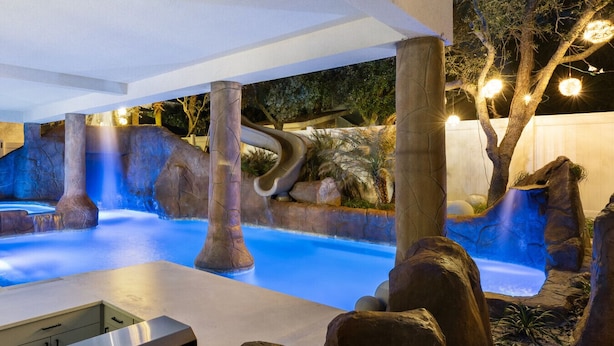 An indoor pool area with rock formations and a slide, surrounded by trees and night lighting. - Gulf views, Saltwater lagoon & waterfall, Beach@2min walk, Firepit, Golf Cart, Elevator (Destin)