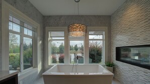 Un baño moderno con una bañera independiente, ventanas amplias y un accesorio de luz decorativo.