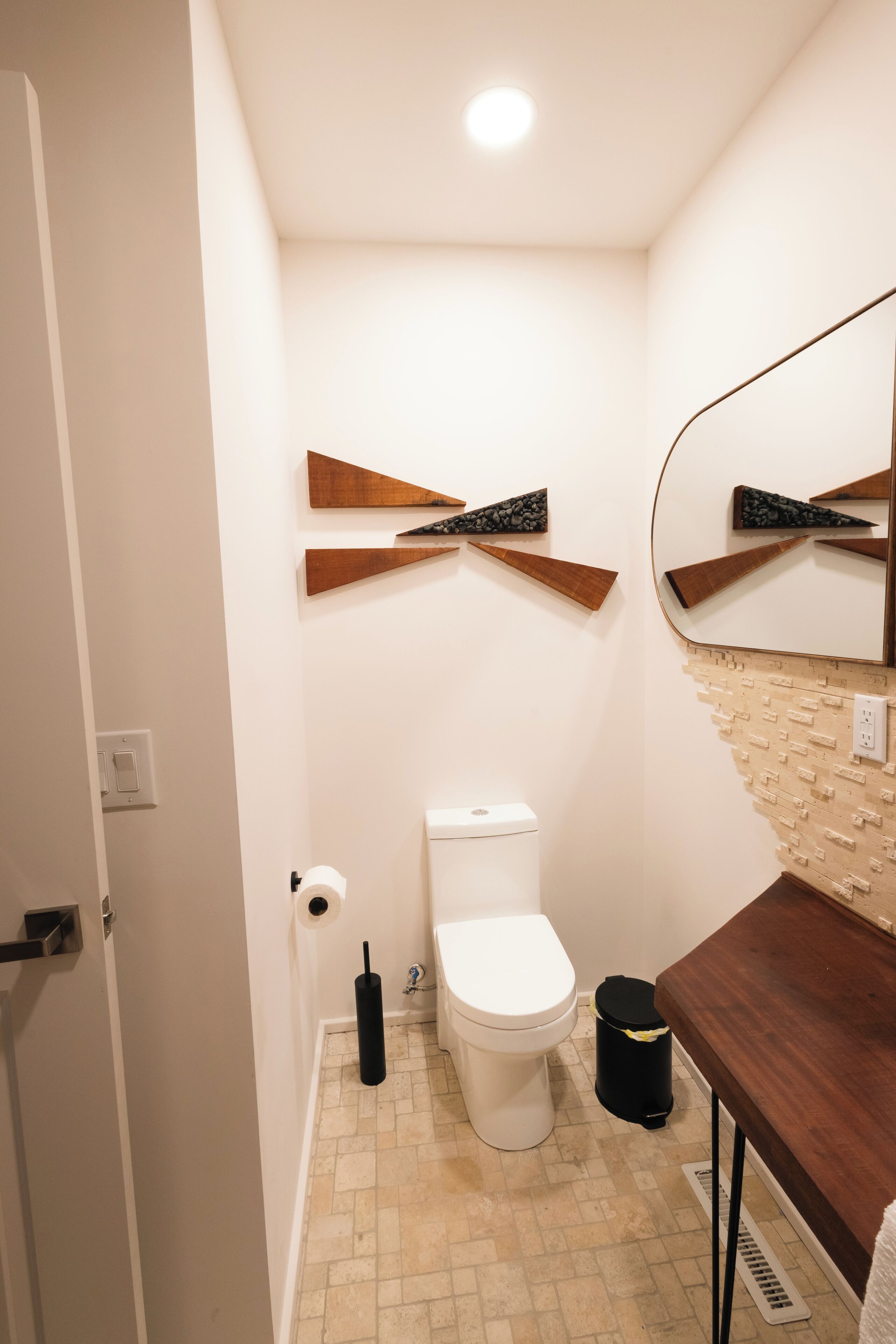 Un baño pequeño con inodoro blanco, un bote de basura negro y un tocador de madera con espejo.