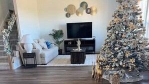 A living room with a wooden floor, a white sofa, a TV, and a Christmas tree. - New house. 20 minutes from ATX, 5 bedrooms (Manor)