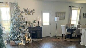 A spacious living room with a large Christmas tree, dark wooden flooring, and a dining area with a table and chairs. - New house. 20 minutes from ATX, 5 bedrooms (Manor)
