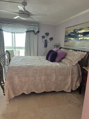A bedroom with a bed, a ceiling fan, a window with curtains, a wall-mounted plant, and a painting. - Cozy beachfront 2-bedroom condo in tranquil Sarasota with AC and laundry in unit (Sarasota)