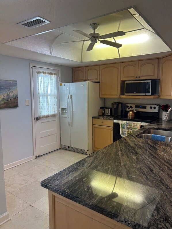 A kitchen with a refrigerator, microwave, stove, and a ceiling fan. - Cozy beachfront 2-bedroom condo in tranquil Sarasota with AC and laundry in unit (Sarasota)