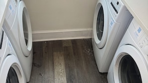 Ein Waschbereich mit zwei Waschmaschinen, die nach vorne geladen werden, einem Holzboden und einer weißen Wand.