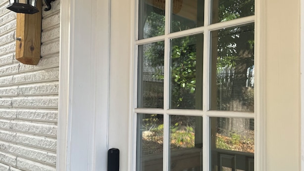 Eine weiße Tür mit Glasfenster, Klingel in Schwarz und ein hölzerner Laternenleuchter an der Wand.