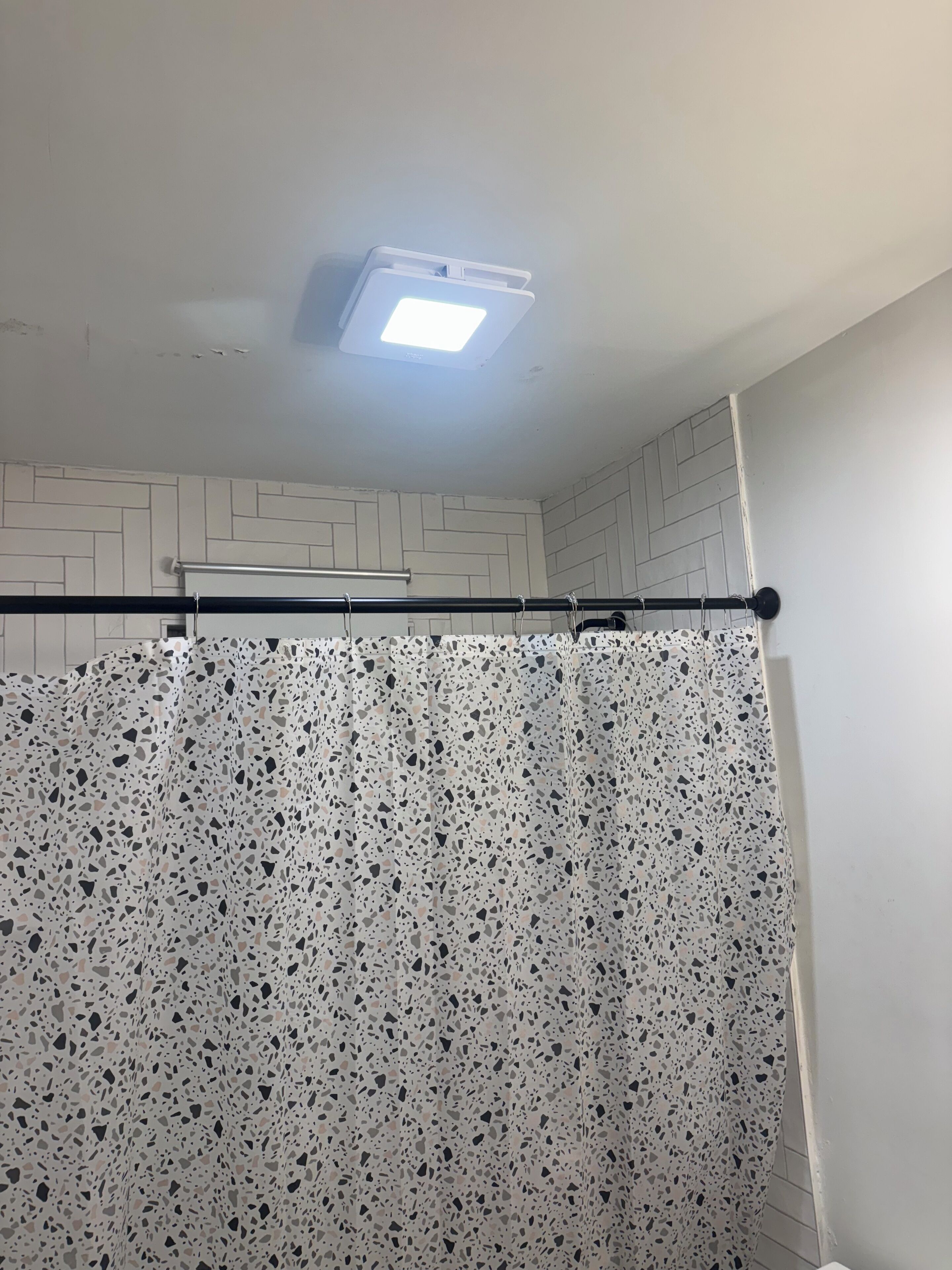 Un baño con cortina de ducha, luz de techo y pared con azulejos.