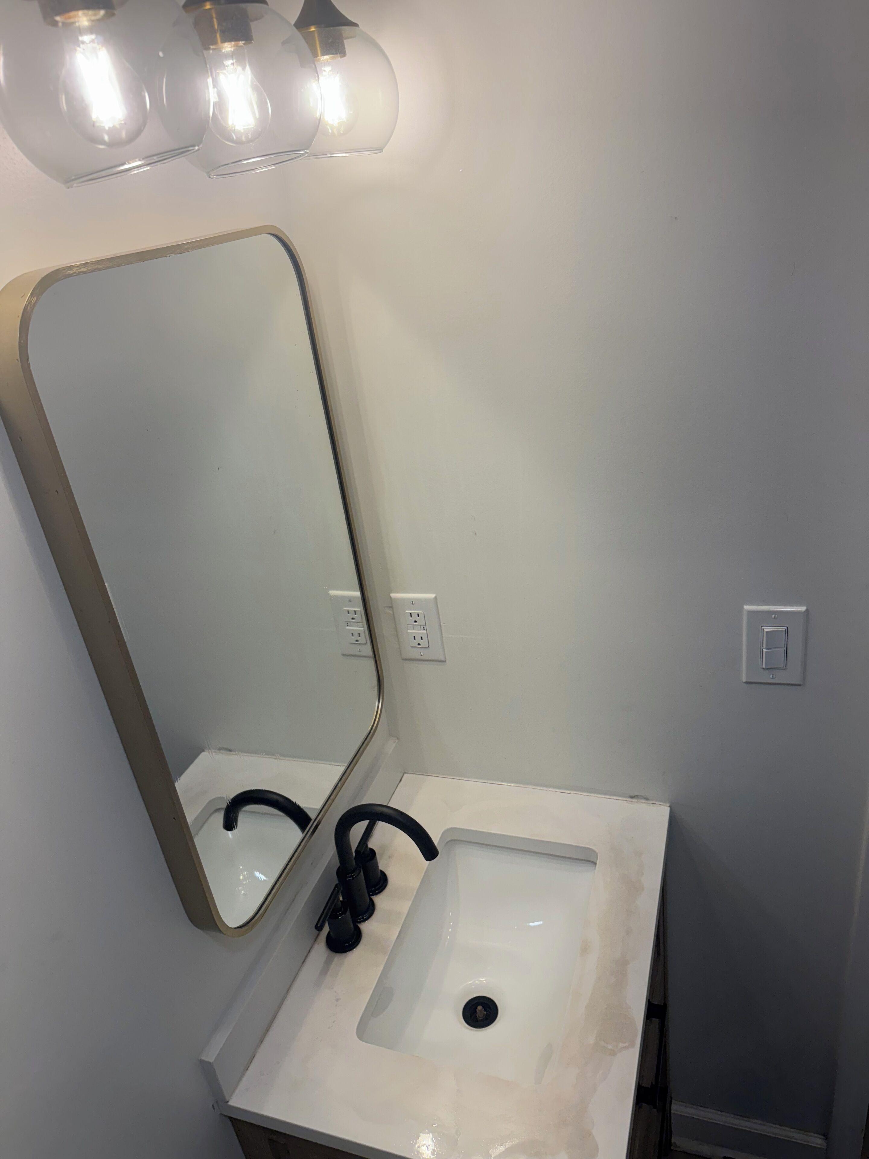 A bathroom with a white sink, a mirror, and a light fixture above the mirror.