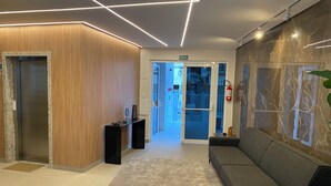 A modern lobby with a wooden reception desk, a black sofa, a marble wall, and a glass door leading to an outdoor area. - Apartment in Ubatuba Tenório. 3 minutes from the beach. (Ubatuba)