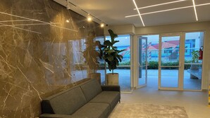 A modern interior with a marble wall, a grey sofa, a round table, and a potted plant. - Apartment in Ubatuba Tenório. 3 minutes from the beach. (Ubatuba)