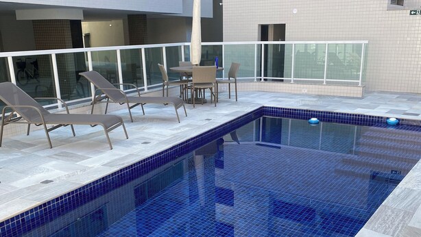 A swimming pool with blue tiles, lounge chairs, and a table with chairs. - Apartment in Ubatuba Tenório. 3 minutes from the beach. (Ubatuba)