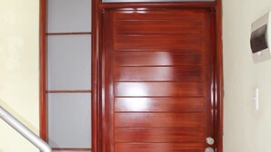 A wooden door with a frosted glass panel, a metal handrail, and a doormat on a tiled floor.