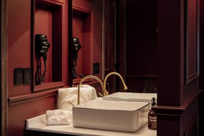 A bathroom with a white sink, gold faucets, a hand soap dispenser, and a hairdryer mounted on the wall. - The Urban Muse suite (Mexico City)