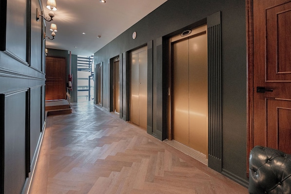 Un pasillo con piso de madera, un banco de cuero negro y un conjunto de ascensores.