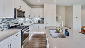 Una cocina moderna con armarios blancos, un lavamanos de acero inoxidable y un microondas.