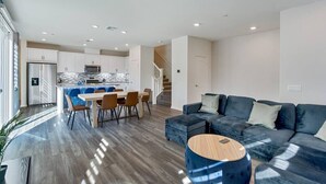 Una sala moderna con un sofá seccional azul oscuro, una mesa de centro de madera y un comedor con una cocina al fondo.