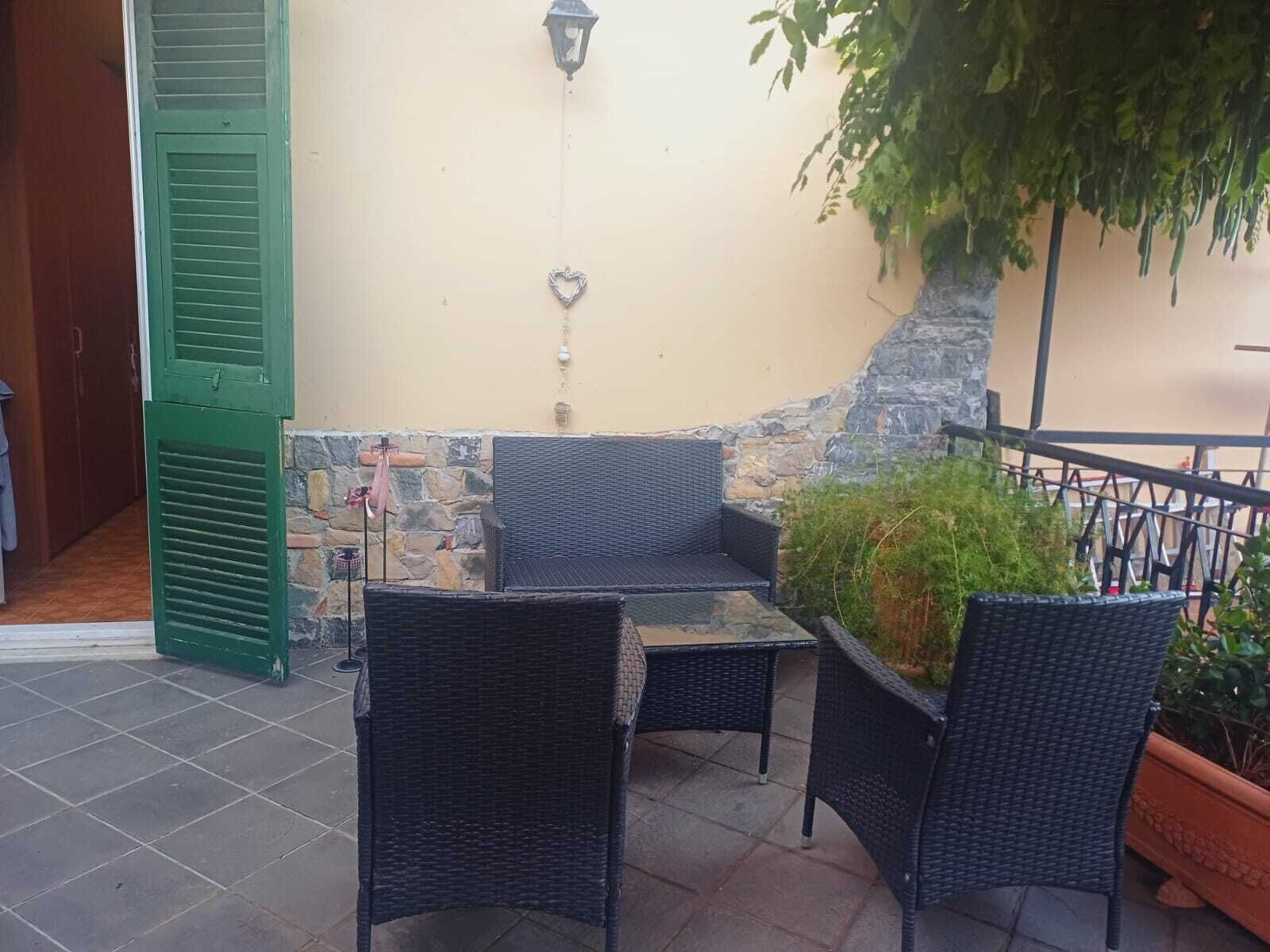 Ein Sitzbereich im Freien mit Korbstühlen und einem Tisch, einer Steinsäule und einer grünen Tür.