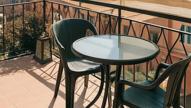Un balcón con una mesa de vidrio y dos sillas, con vista a una masa de agua y tierra distante.