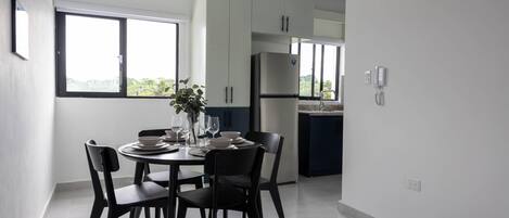 Una cocina moderna con armarios blancos, un refrigerador de acero inoxidable y un comedor con una mesa redonda y cuatro sillas.
