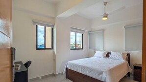 Een ruime slaapkamer met een groot bed, een plafondventilator en een bureau.
