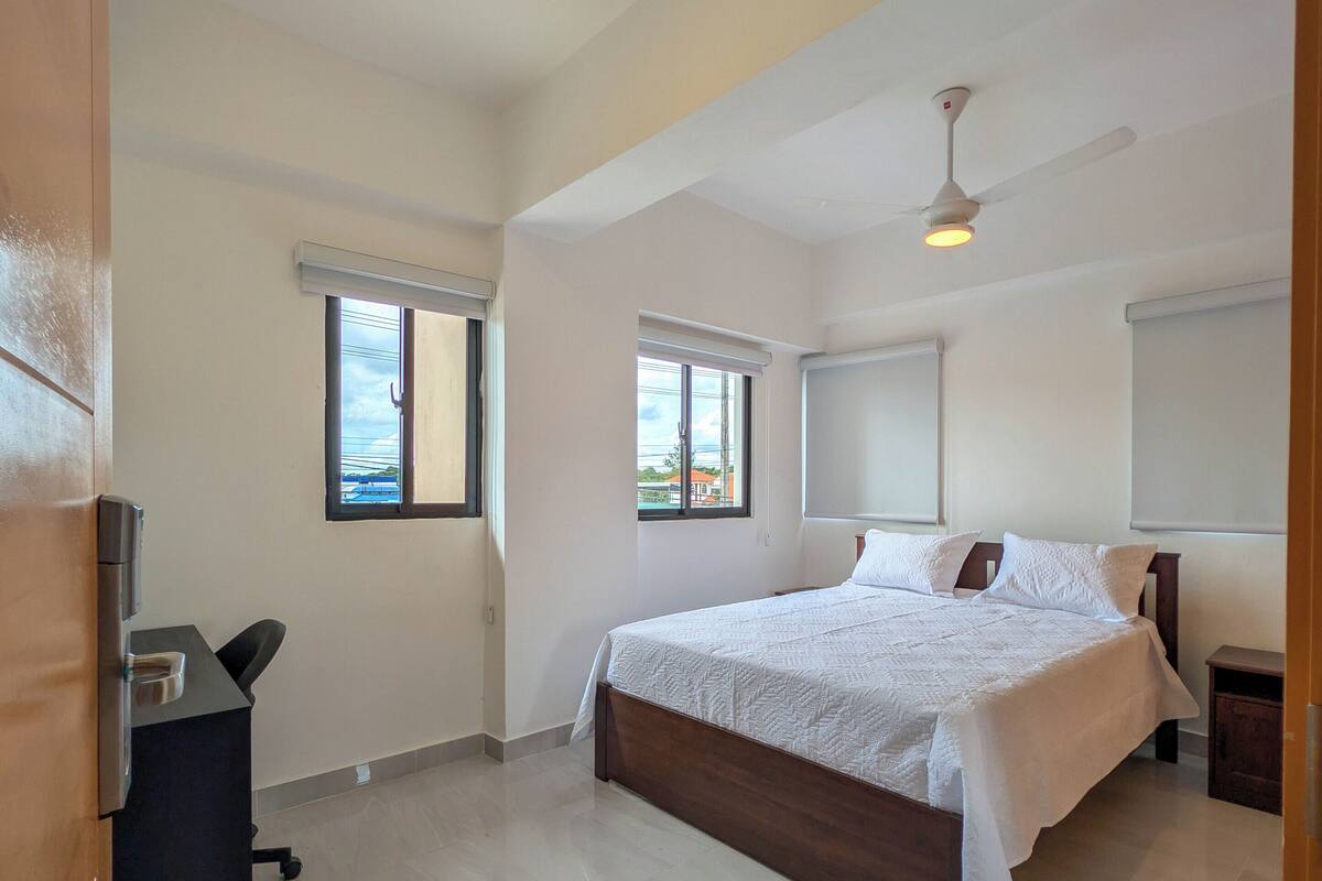 A spacious bedroom with a large bed, a ceiling fan, and a desk.